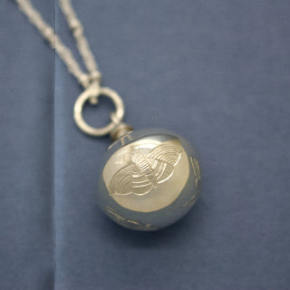 Psyche silver orb pendant, engraved with four butterflies and a single moth, resting on a dark background. British jewellery designer, hand engraver, Emily Proudfoot jewelry.