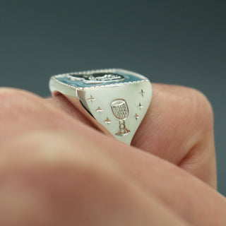 Silver signet ring top face with etched stars and a lantern-like emblem