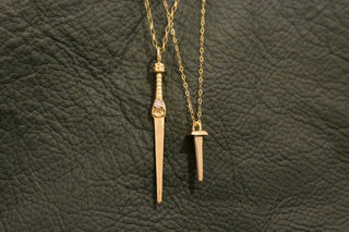Gold and diamond dagger-shaped necklace with coffin nail pendant necklace on dark green leather background - British fine jeweler - Emily Proudfoot