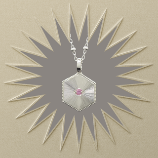 A silver hexagonal pendant necklace with a small pink gemstone in the center, displayed against a textured beige background with a starburst graphic.