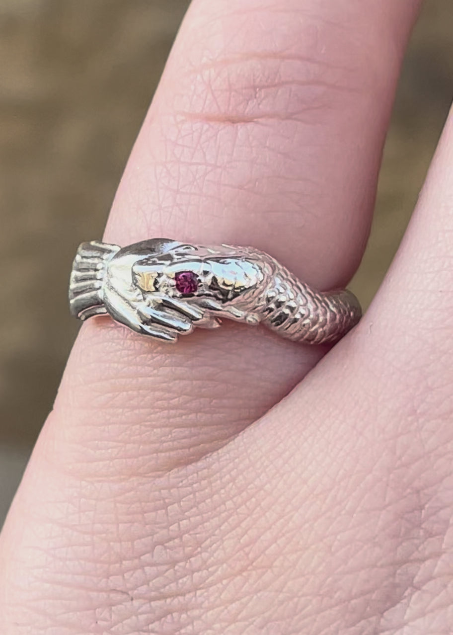 Hand wearing a silver snake  hand shake fede wedding band ring ruby birthstone set eye, inspired by victorian and medieval commitment jewellery - emily proudfoot