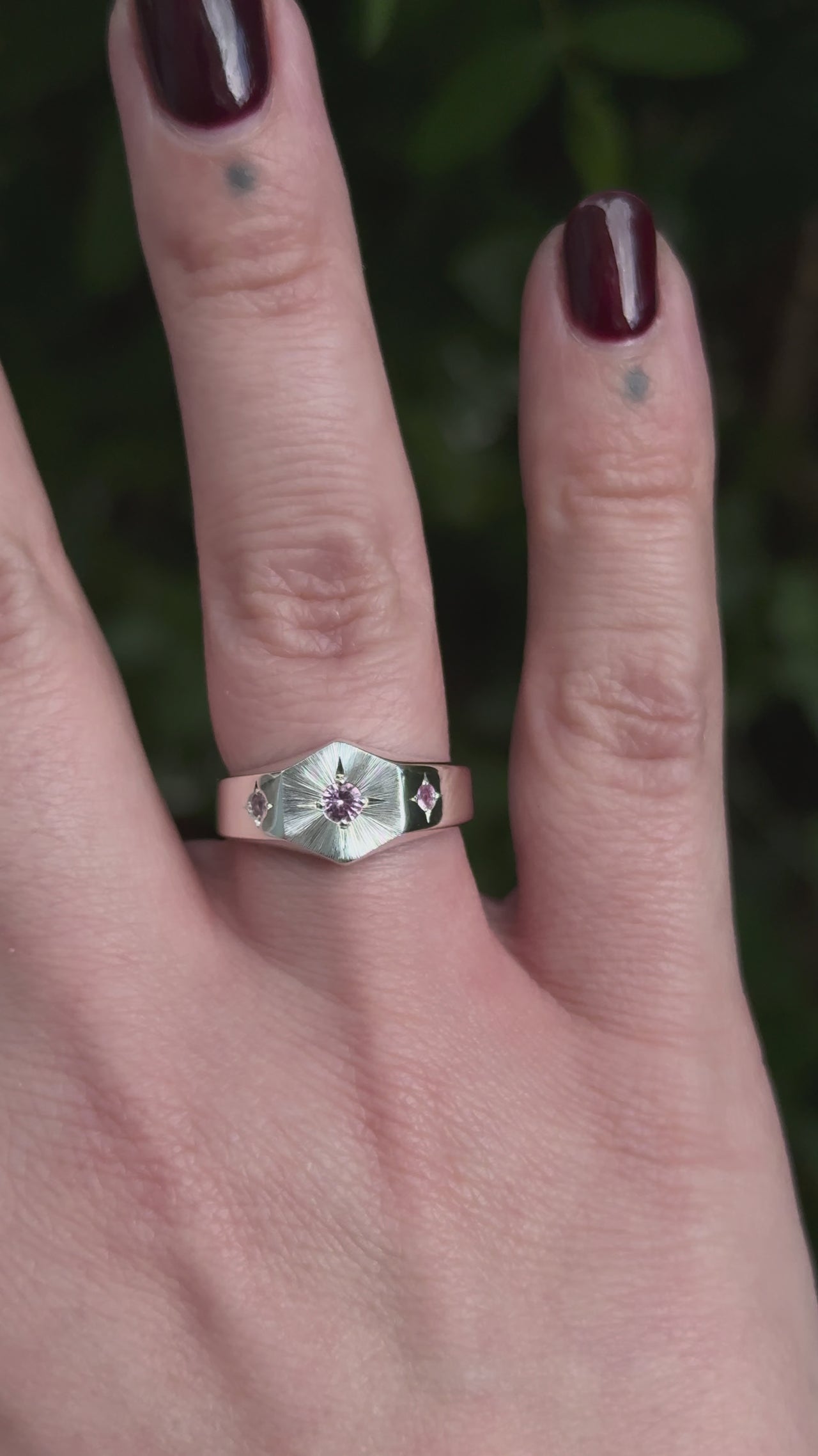 Video of a silver hexagon signet ring with a central natural pink round sapphire gemstone and smaller side sapphire gemstones set in decorative 4 point star settings. The face of the ring is finished with a bright cut hand engraved Guilloché  sunray pattern. Perfect alternative engagement or wedding ring - Emily Proudfoot 